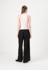 Top de manga cava rosa claro e calças pretas largas. O top tem uma textura canelada, enquanto as calças têm um acabamento suave e pernas largas.