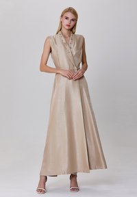 Robe sans manches en satin beige au design enveloppant, texture scintillante, boutons décoratifs et jupe longue.