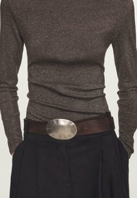 Sprankelend donkerbruin shirt met lange mouwen, gecombineerd met een brede bruine leren riem met een grote zilveren ronde gesp.