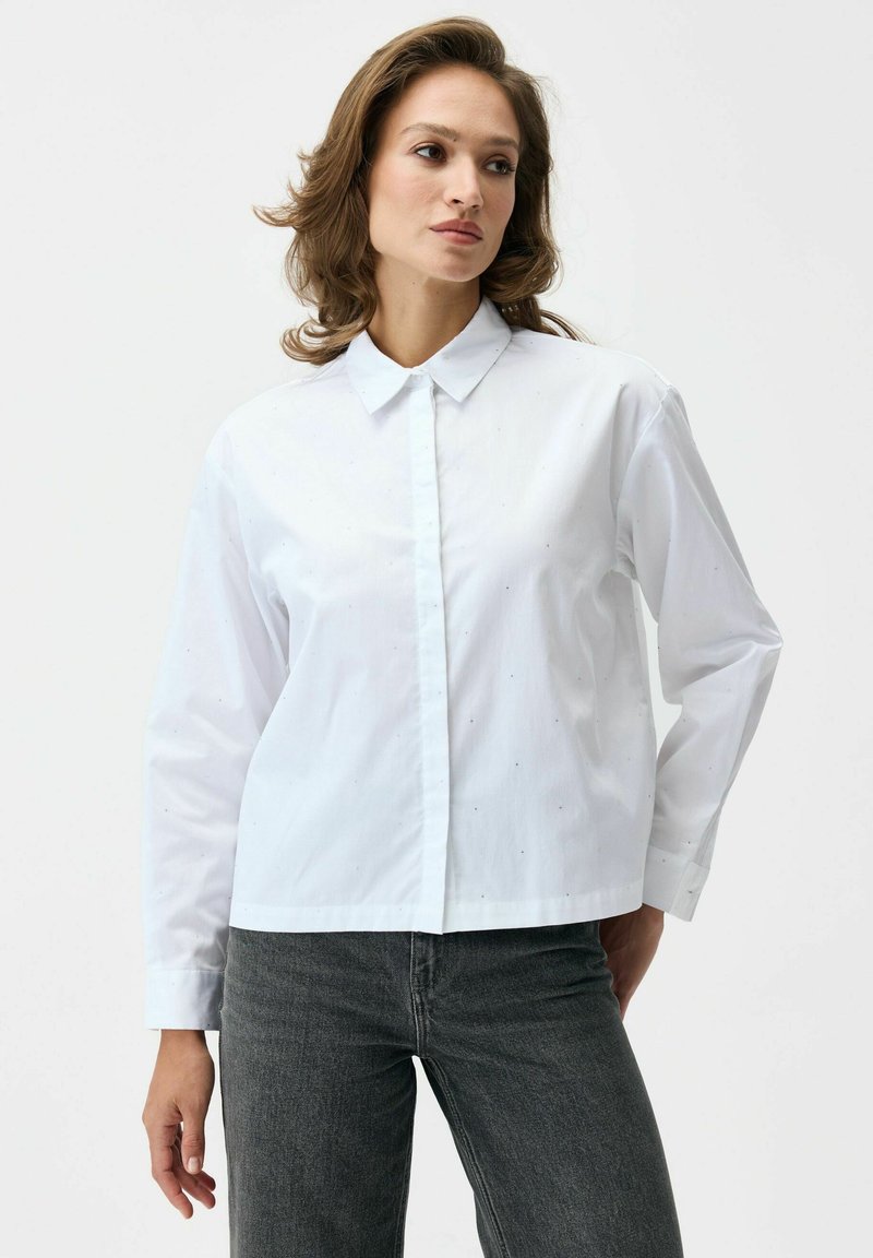 Biała bawełniana koszula z kołnierzykiem, zapięciem na guziki z przodu, długimi rękawami oraz drobnymi tonowanymi kropkami na całej powierzchni.