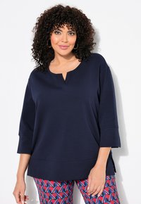 Maglietta a maniche lunghe blu navy con scollo rotondo e un piccolo taglio; abbinata a leggings con motivo a forma geometrica in rosso e blu.