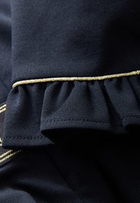 Marineblauwe stof met een getextureerd oppervlak, voorzien van gerimpelde ruches langs de rand, geaccentueerd met een dunne metalen gouden bies.