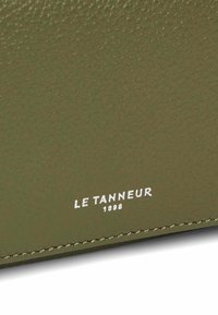 Cartera de cuero texturizado color verde oliva con el logotipo en relieve "LE TANNEUR 1898" en blanco, que presenta una costura precisa en los bordes.