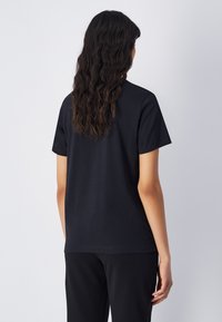 Maglietta in cotone nera con maniche corte e vestibilità rilassata, texture liscia, senza motivi o dettagli, vista da dietro.