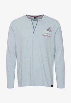 Svijetloplava košulja dugih rukava s henley izrezom, dva dugmeta na pritisak i grafikom na prsima u crvenoj i tamnoplavoj boji. Mekani pamučni materijal, ležeran dizajn.