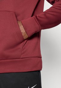 Raudonas džemperis su kišenėmis, guminėmis rankovėmis ir lygia, tekstūrine medžiaga. Derinamas su juodomis kelnėmis ir subtiliu logotipo medžiagu.