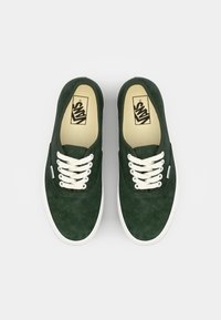 Grüne Wildledersneaker mit weißen Schnürsenkeln und Gummisohlen. Auffälliges Vans-Logo auf der Innensohle und ein minimalistisches Design.