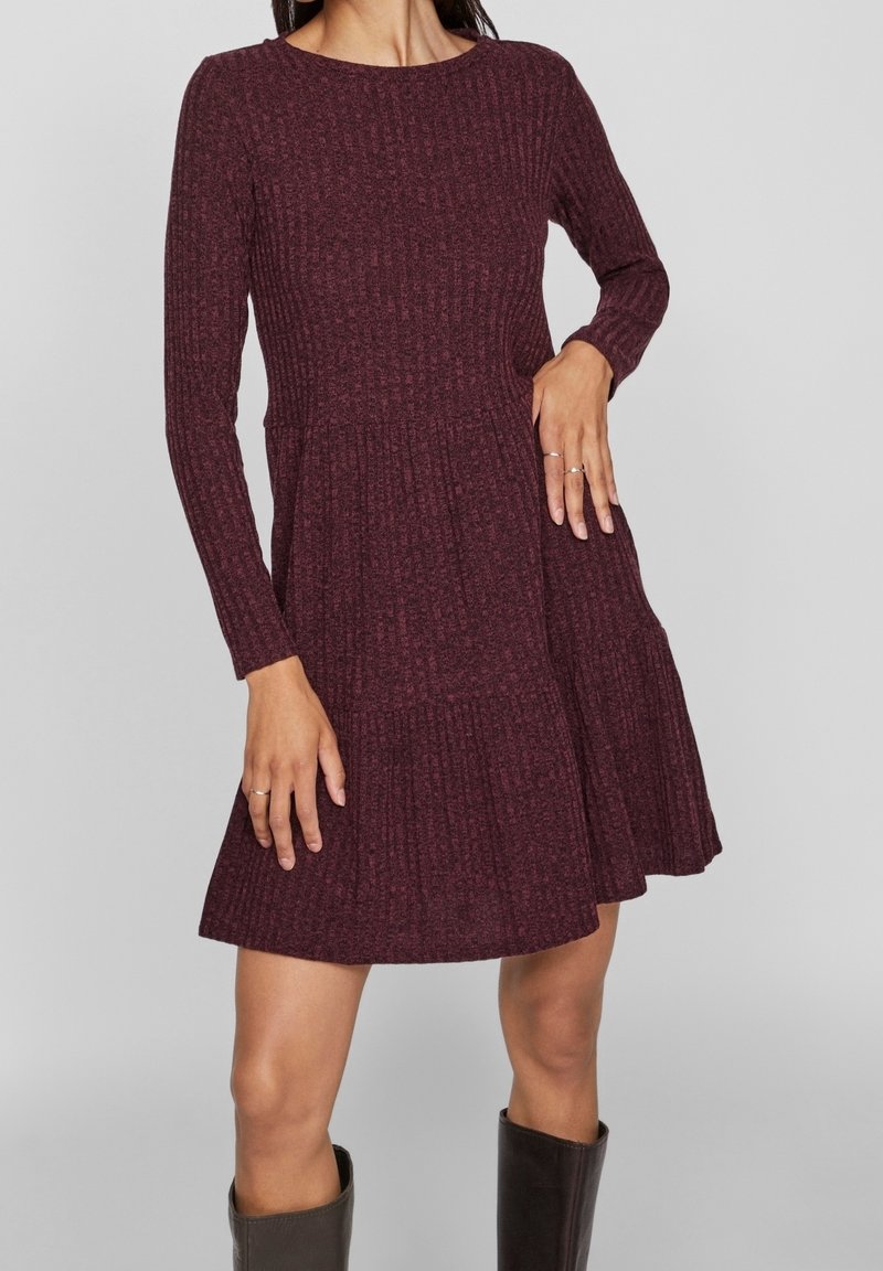 Burgundské páskované šaty s dlouhými rukávy, kulatým výstřihem a rozšířenou sukní; tkanina s texturou a sklady v oblasti pasu.