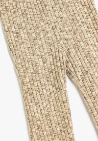 Leggings a coste in beige chiaro con strisce più scure. Texture morbida, forma aderente e vita elastica, ideali per un look casual.