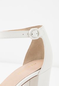 Weiße High-Heel-Sandale mit einem glatten Lederoberteil und einer samtigen beige Innensohle. Sie besitzt eine runde Zehenpartie, einen Knöchelriemen und einen breiten Blockabsatz.