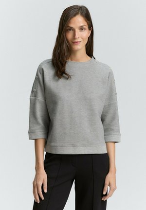 Grijze sweatshirt met textuur, een ronde hals en driekwart mouwen, met knopenaccenten op de schouders. Draag het met zwarte broeken.