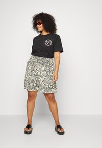 T-shirt preto de manga curta com gráfico "NYC", combinado com uma saia com padrão floral em tons de rosa e verde, e sandálias pretas.