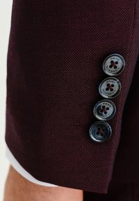 Bordowy materiał teksturowany o gładkim wykończeniu, z czterema guzikami na rękawie, z wytłoczonym napisem "PAKO LORENTE" w kolorze czarnym.