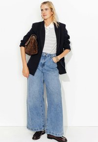 Un jean en denim bleu taille ample associé à un blazer noir et un polo à rayures blanches. Un sac à main en imprimé léopard brun complète la tenue.