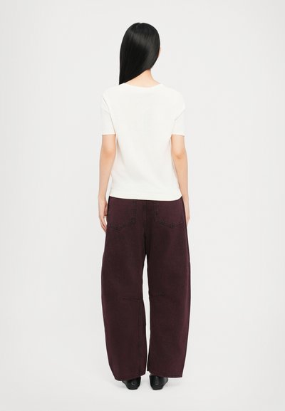 Top aderente bianco a maniche corte abbinato a pantaloni larghi bordeaux scuro, caratterizzati da tasche posteriori ben definite e una silhouette rilassata.