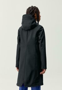 Črna jakna s prilegajočim dizajnom, kapuco in dolgimi rokavi. Ima šive in zareze na robu. Gladka tekstura tkanine.