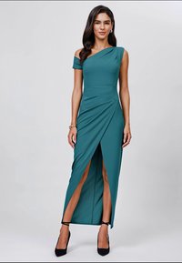Teal off-shoulder dress with a fitted bodice and draped waist. Features a high slit on one side and a smooth, stretchy fabric. Black heels.