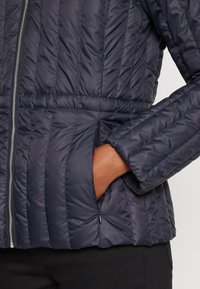 Marineblauer Puffer-Jacke mit gestepptem Muster, Reißverschluss Vorderseite und seitlichen Taschen. Elastischer Bund und Bündchenärmel sorgen für Struktur und Form.