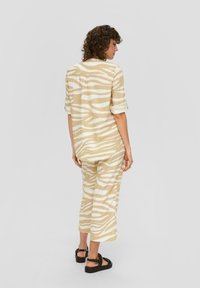 Beige- und weiß gestreiftes Oberteil und passende Hose aus leichtem Material. Bequeme Passform mit umgeschlagenen Ärmeln und knöchellangen Hosen. Schwarze Sandalen.