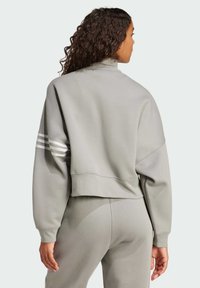 Sudadera gris recortada con un alto cuello, mangas largas y tres franjas blancas en el brazo izquierdo. Tejido suave con un corte relajado.