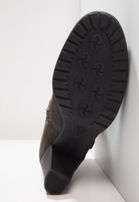 Botte en daim marron avec une semelle en caoutchouc noire texturée présentant un motif de sculptures circulaires et un talon empilé bas.