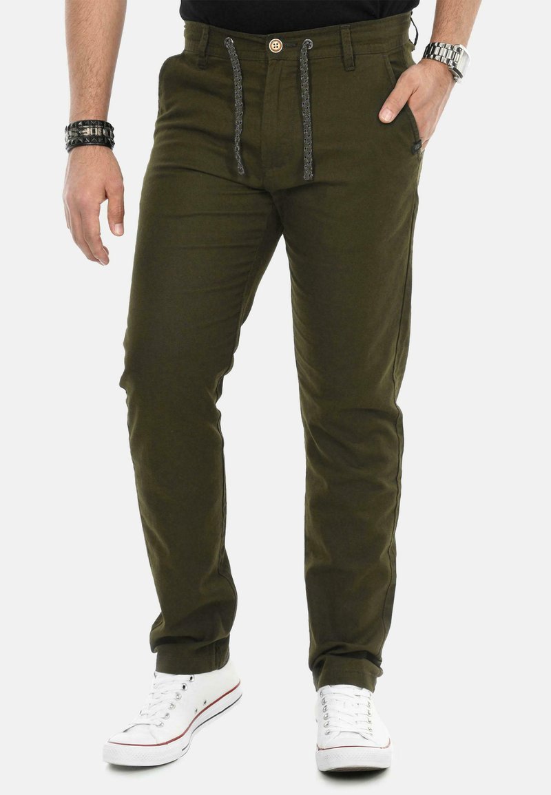 Olive green cotton pants featuring a drawstring and button closure, straight legs, side pockets, and white sneakers with red accents.