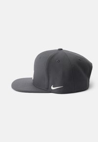 Črna bejzbol kapa iz mešanice bombaža. Ima ravno vizir in izvezeno belo Nike logo na strani. Šestpanelna zasnova.