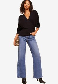 Zwarte wikkeltrui met een diepe V-hals, gecombineerd met wijde blauwe denim jeans en zwarte puntige enkellaarsjes. Inclusief een clutch met panterprint.