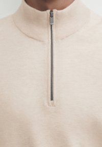 Close-up of a beige zip-up sweater collar with a partially zipped small black zipper.