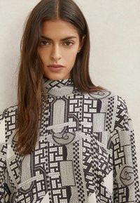 Langærmet top med høj hals, sort-hvidt geometrisk mønster og glat stofstruktur.