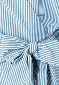 Tessuto a righe blu e bianche con una texture morbida, caratterizzato da un dettaglio a fiocco legato in vita. Le righe sono equidistanti e simmetriche.