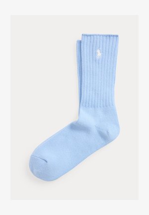Chaussette en coton bleu clair côtelée avec un logo brodé d'un joueur de polo blanc près de la bordure, présentée à plat sur un fond blanc.