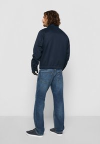 Marineblå bomberjakke med høy krage, paret med lyseblå jeans. Denim har et klassisk fem-lommer design og liten falming.