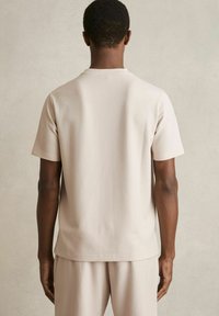 Kortærmet skjorte i lys beige med et struktureret ribbet design. Har en rund halsudskæring og lige snit, parret med løse matchende bukser.
