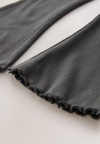 Dark gray ribbed fabric with a flared hem featuring a ruffled edge. The texture is soft, and the design shows vertical stripes.