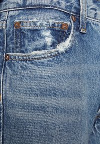 Jeans de mezclilla azul claro con un bolsillo trasero desgastado, con bordes deshilachados y remaches de cobre. La textura es suave con un patr�ón descolorido.