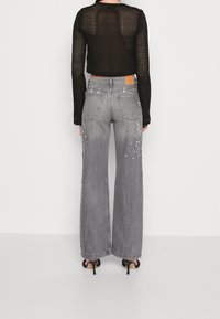 Un pull en maille noir court associé à un jean ample gris. Le jean présente des détails de éclaboussures et des poches arrière, avec une légère déchirure au niveau de l'ourlet.