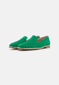 Scarpe slip-on in suede verde con punta arrotondata, cuciture minime e un accento dorato sul bordo della suola.