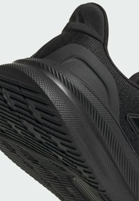 Chaussure de sport noire avec une tige en maille texturée, semelle en caoutchouc et semelle à motifs. Présente un talon incurvé et des accents renforcés pour le soutien.
