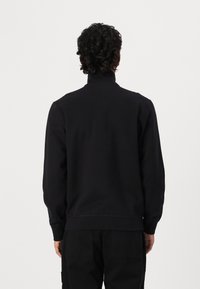 Felpa nera con collo alto, polsini e orlo a costine. Design semplice, realizzata in tessuto morbido, senza loghi o motivi visibili.