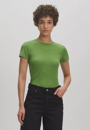 Grünes geripptes T-Shirt mit kurzen Ärmeln und Rundhalsausschnitt, kombiniert mit hochsitztenden schwarzen Jeans. Glatte Textur, taillierte Passform.