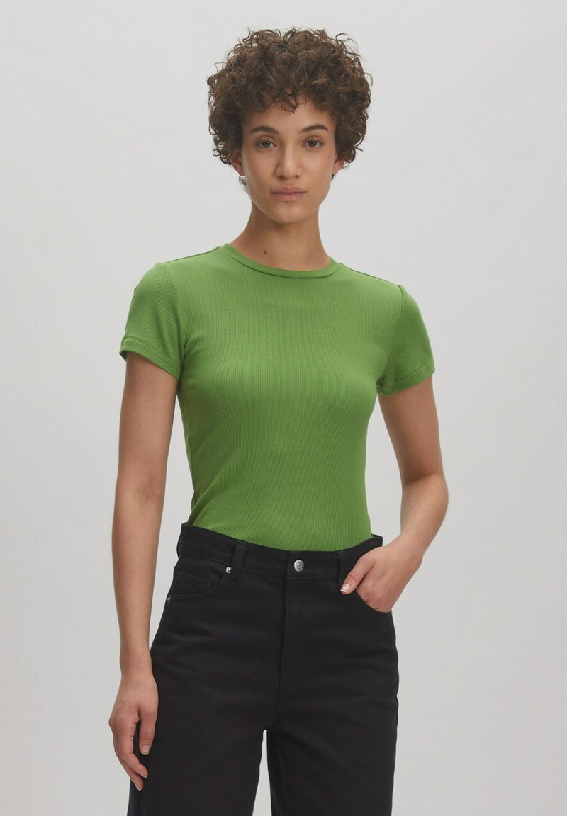 Groene geribde t-shirt met korte mouwen en een ronde hals, gecombineerd met hoge taille zwarte jeans. Glad textuur, strakke pasvorm.