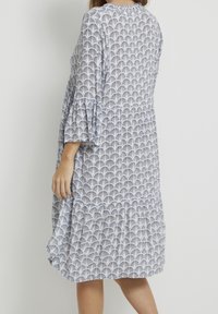 Blå mönstrad klänning i mjukt, lätt tyg, med fläktade ärmar och lager-på-lager nederdel, som visar en fläktliknande print.