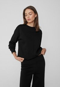 Czarny sweatshirt wykonany z miękkiego materiału, z prostym, okrągłym dekoltem i długimi rękawami. Tekstura jest gładka z subtelnym detalem szwów.