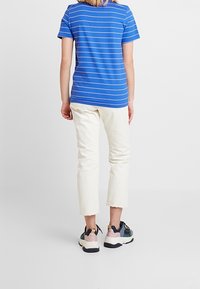 Niebieski t-shirt w paski z krótkim rękawem, zestawiony z białymi, skróconymi spodniami oraz czarnymi, wielokolorowymi trampkami. Charakterystyczny detal wykończenia na nogawkach spodni.