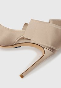 Μπεζ σατέν πέδιλο με ψηλό τακούνι, λουράκι στον αστράγαλο και ανοιχτά δάχτυλα, σε λευκό φόντο, παρουσιάζοντας λεπτό τακούνι στιλέτο και ομαλή υφή.