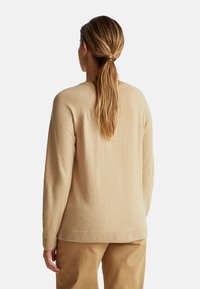 Beżowy sweter o miękkiej teksturze, z okrągłym dekoltem i raglanowymi rękawami. Posiada ściągacze na mankietach i u dołu, zestawiony z khaki spodniami.