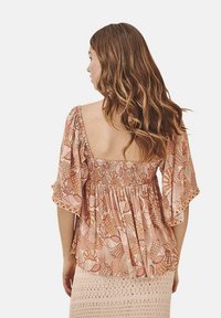 Blusa estampada en melocotón y beige con la parte trasera fruncida, mangas cortas y un escote profundo. Llevada sobre una falda de ganchillo clara.