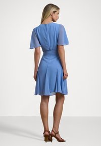 Ανοιχτό μπλε φόρεμα με κοντά φουσκωτά μανίκια, εφαρμοστό μέσο και φαρδύ φούστα. Φερμουάρ στην πλάτη και ρέουσα ύφανση με λεία υφή.