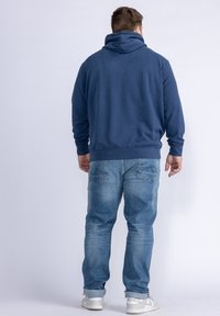 Felpa blu navy con colletto alto, maniche lunghe e vestibilità comoda, abbinata a jeans in denim azzurri e scarpe da ginnastica bianche.